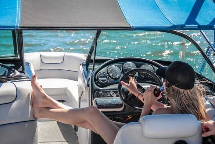 A young girl is driving a yacht while drinking.